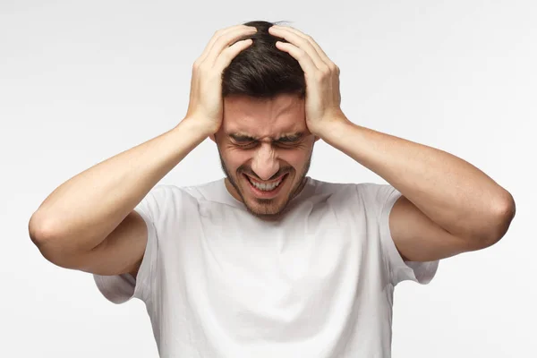 Giovane infelice sconvolto in t-shirt bianca che stringe la testa con le mani, soffre di mal di testa. Persone, stress, tensione ed emicrania — Foto Stock