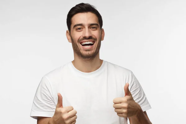 Jeune homme optimiste isolé sur fond gris montrant des coups de pouce avec des émotions positives de contenu et de bonheur. Concept de satisfaction à l'égard de la qualité et recommandation — Photo