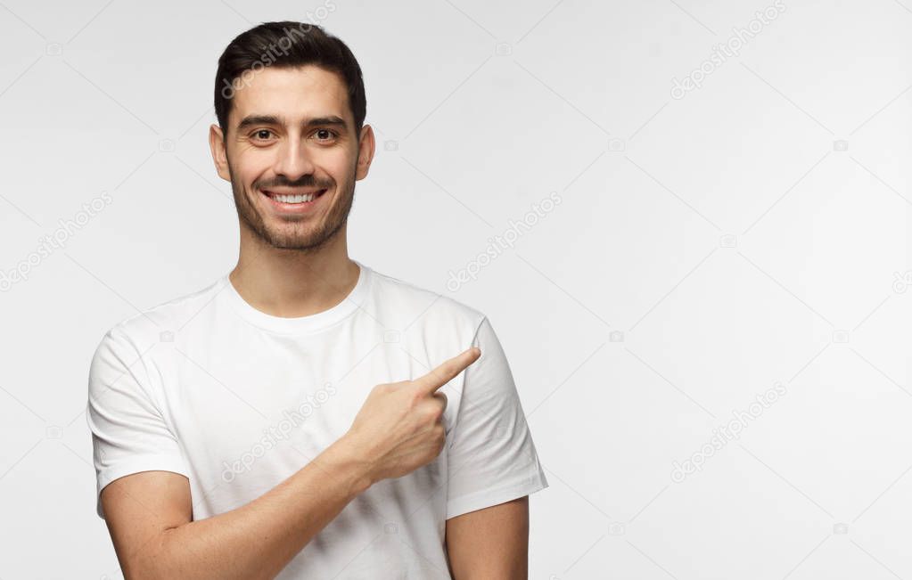 Attractive young man in white t-shirt pointing right with his finger isolated on gray background