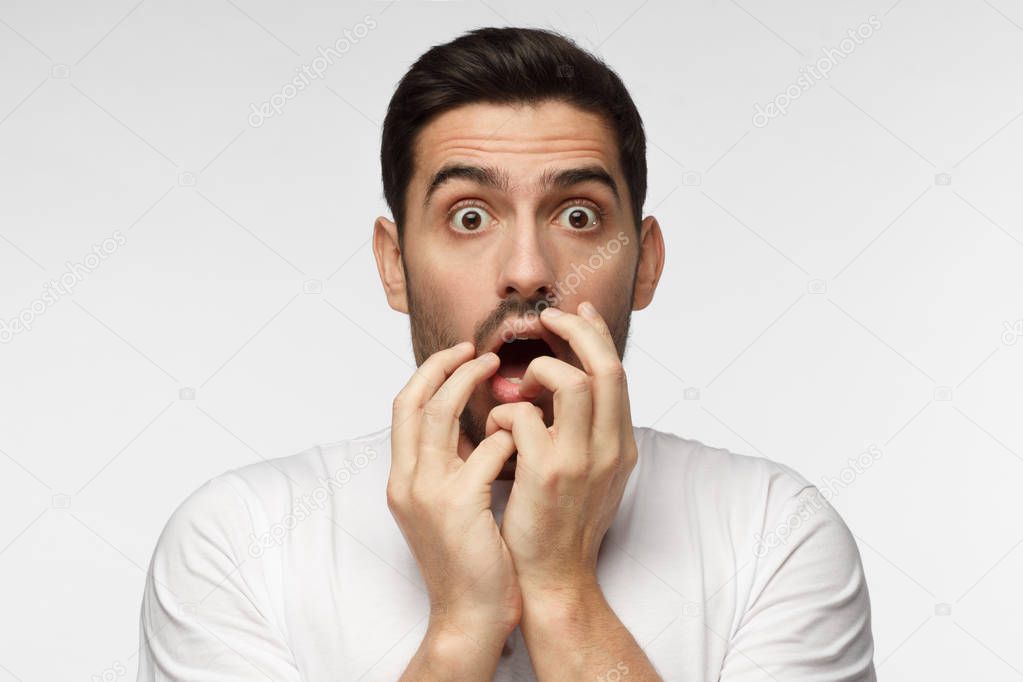 Astonished bug-eyed man covering his mouth with both hands, looking shocked. Surprised, embarrassed and confused young male showing omg emotion