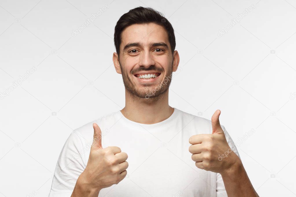 Motivated excited young man in white tshirt making a thumbs up gesture of approval and success with smile