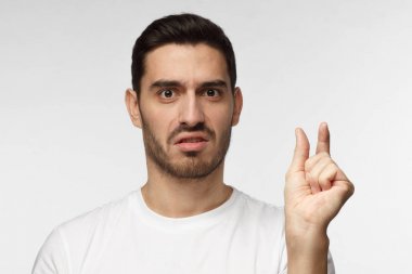 Çok minik! Beyaz tshirt, genç adam gesticulates elleri ile küçük boyut unpleased yüz ifadesi ile gösterilen