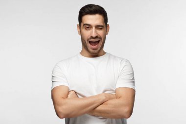 Genç atletik sportif adam gülümseyerek ve göz kırpıyor, kameraya bakarak çapraz kolları olan 