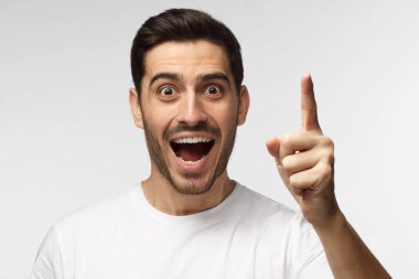 I got a eriyik! Büyük yenilik düşünce sahip beyaz tshirt işaret parmak eureka işareti, gri arka plan üzerinde izole giyen enerjik güzel gülümseyen adam fotoğrafı