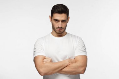 Ciddi genç adam portresi. Sert çocuk çapraz kolları üzerinde gri arka plan izole olan ayakta