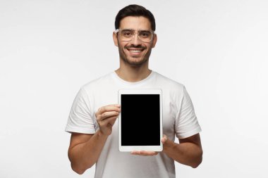 Boş tablet ekran sunan bir gülümseme ile izleyiciler, boşaltmak için reklam mal veya apps için resimde izole üzerinde gri arka plan ile trendy şeffaf gözlük, genç adam