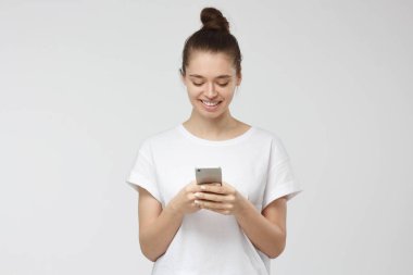 Açıkça smartphone her iki elinde tutarken gülümseyen yakışıklı genç kadının smartphone vasıl seyir gri arka plan üzerinde izole kapalı atış