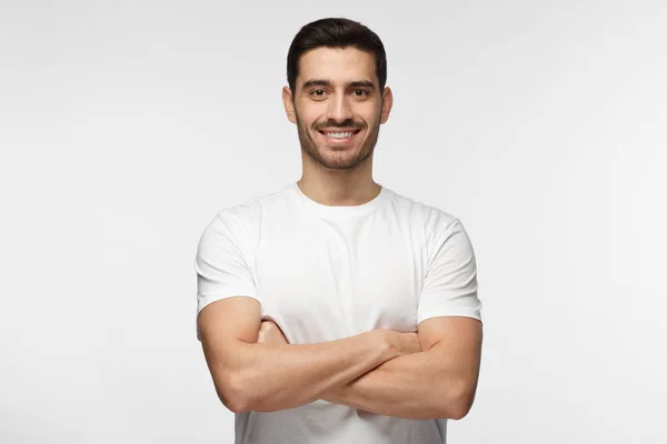 Retrato de hombre guapo sonriente en camiseta blanca de pie con brazos cruzados aislados sobre fondo gris — Foto de Stock