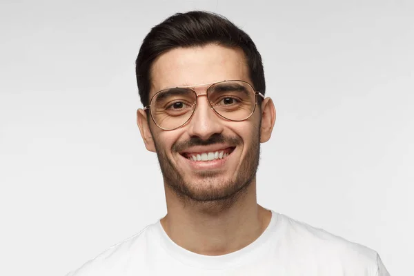 Close up retrato de homem bonito sorridente em óculos da moda e t-shirt branca isolada no fundo cinza claro — Fotografia de Stock