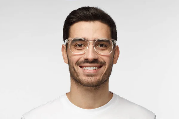 Close-up shot van de glimlachen van aantrekkelijke man in de witte t-shirt en trendy trasparent brillen geïsoleerd op een grijze achtergrond — Stockfoto