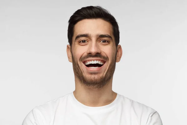 Close up horizontal tiro de belo homem jovem sem barba em tshirt branca rindo em voz alta, sorrindo amplamente — Fotografia de Stock