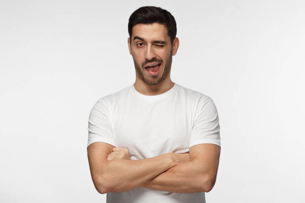 Studio shot of good looking man isolated on grey background looking enterprising and enthusiastic, winking friendly as if inviting to adventure or recommending good benefit