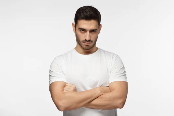 Sérieux portrait de jeune homme. Dur gars debout avec les bras croisés isolé sur fond gris — Photo