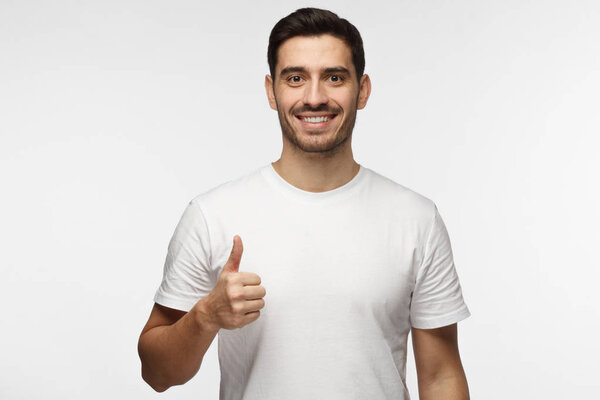 Young optimistic man isolated on grey background showing thump up with positive emotions of content and happiness. Concept of satisfaction with quality and recommendation
