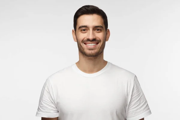 Ritratto ravvicinato di un bell'uomo sorridente in t-shirt bianca che guarda la macchina fotografica, isolato su sfondo grigio — Foto Stock
