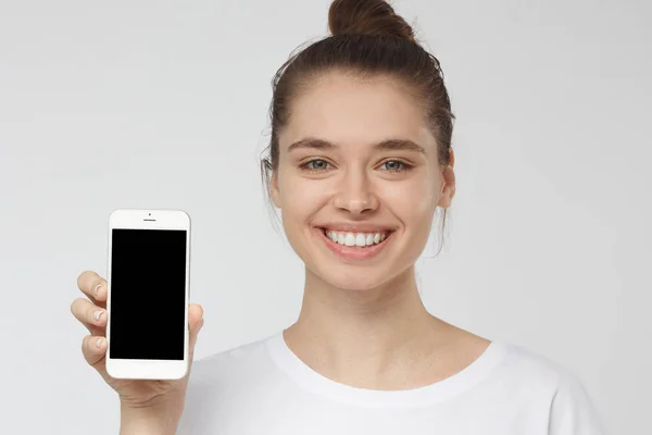 Fecho da jovem mulher sorrindo e segurando e mostrando smartphone em branco com copyspace para publicidade de aplicativos, sites, bens e serviços — Fotografia de Stock