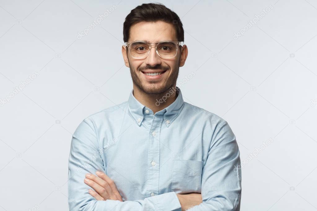 Portrait of smiling handsome business man in casual blue shirt standing with crossed arms isolated on gray background