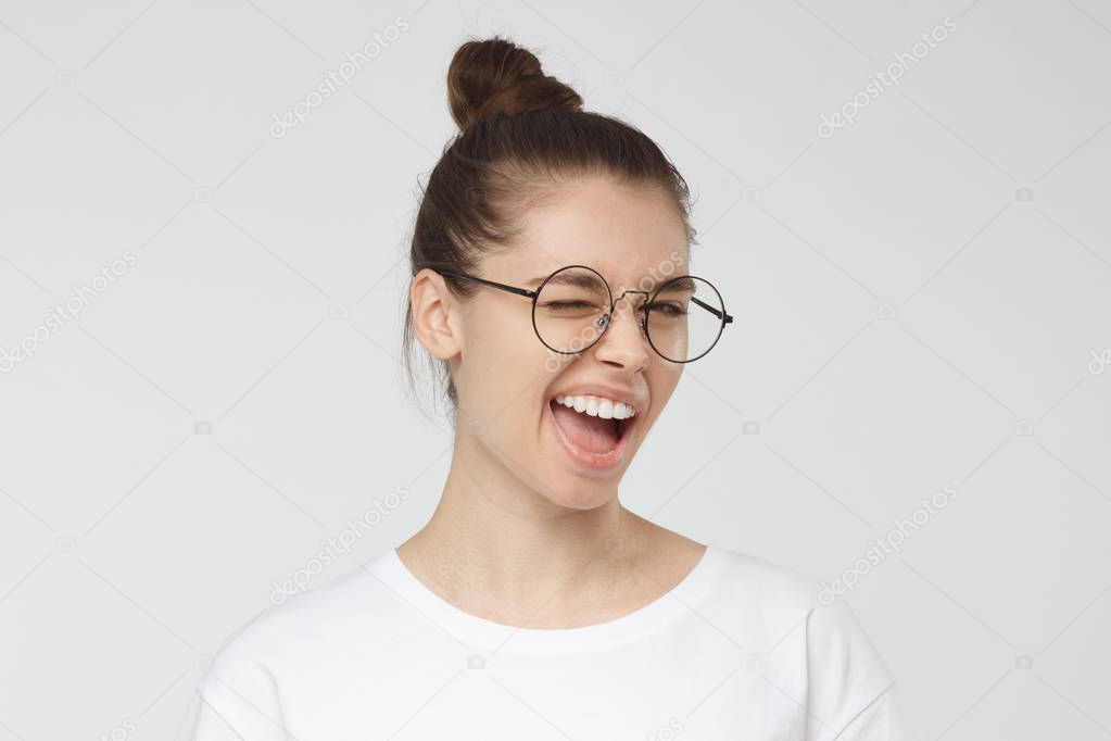 Young woman in round spectacles smiling and winking, looking at camera