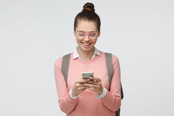 Close up retrato filmado de jovem isolada em fundo cinza, olhando agitado em exibição de seu smartphone sorrindo e rindo alegremente, impressionado com o conteúdo de mídia da web — Fotografia de Stock