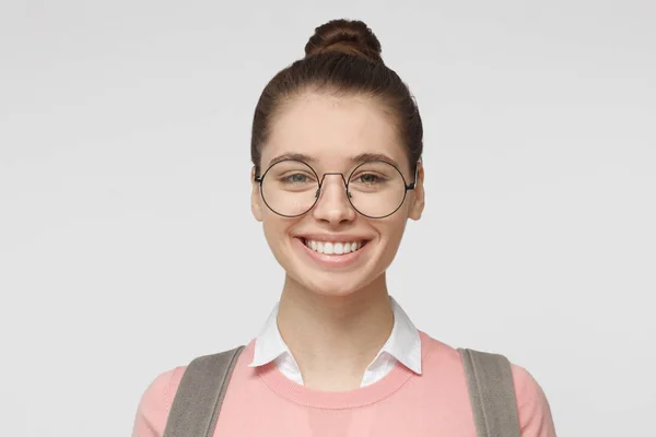 Primer plano de joven mujer guapa en gafas aisladas sobre fondo gris en suéter rosa y camisa blanca con cuello, mostrando sonrisa amistosa, lista para participar en la comunicación — Foto de Stock