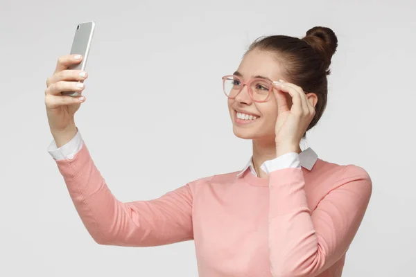 Foto de jovem fêmea isolada em fundo cinza, esticando o braço com smartphone para tirar foto de selfie para compartilhá-la em redes sociais — Fotografia de Stock