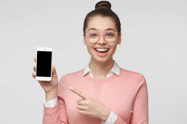 Šťastné mladé samice izolované na šedém pozadí prokázání prázdné smartphone a přejdete na obrazovku s výrazem radosti a zájmu. Copyspace pro reklamní produkty a služby. — Stock fotografie