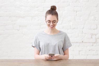 Her iki elinde neşeli kadın girişimci holding smartphone, gülümsüyor hoş, tahta masada oturur. Kişi, iş ve iş kavramı. 