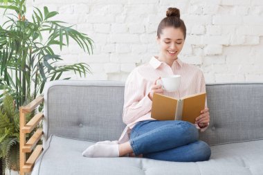 Genç mutlu kadın evde, kanepede rahatlatıcı ilginç eski kitap okuma