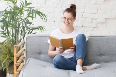 Mutlu genç hipster kadın modern loft iç kanepe evde, hikaye kitabı okuma