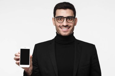 Gri arka plan üzerinde izole yakışıklı sofistike iş adamı boşaltmak için reklamları ile akıllı telefon ve gösteren boş siyah perde göstermek