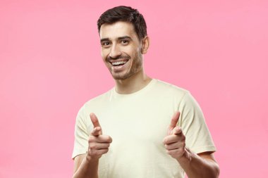 Hey siz! Genç adam kameraya, pembe arka plan izole parmaklarıyla işaret