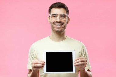 Tablet tutarak ve ürün veya hizmet danışmanlık sanki boş ekran mutlu gülümseme ile gösterilen rahat kıyafetler içinde duran pembe arka plan üzerinde izole olumlu adam stüdyo resmi