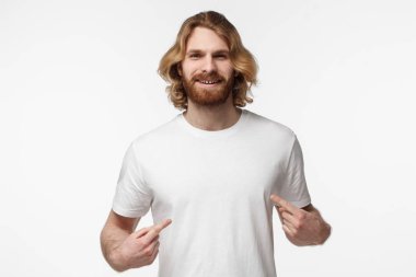 Onun boş beyaz tshirt kopya alanı için reklam, her iki işaret parmakları ile işaret gülümseyen güzel adam gri arka plan üzerinde izole