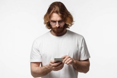 Sakallı genç adam onun arkadaşına mesaj yazarak yuvarlak gözlük, smartphone vasıl seyir gri arka plan üzerinde izole kapalı atış