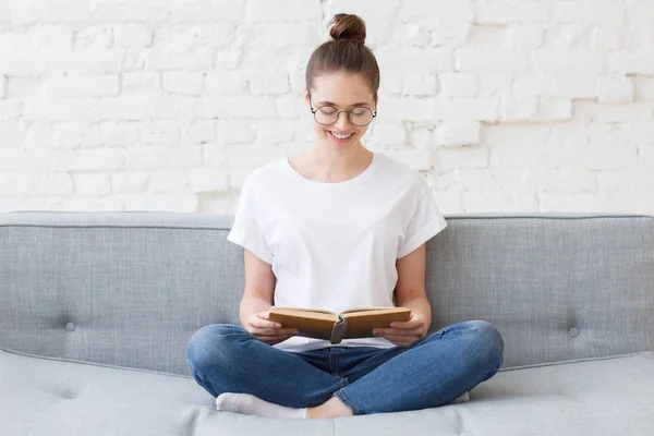 Joven mujer feliz sonriente leyendo en el sofá —  Fotos de Stock