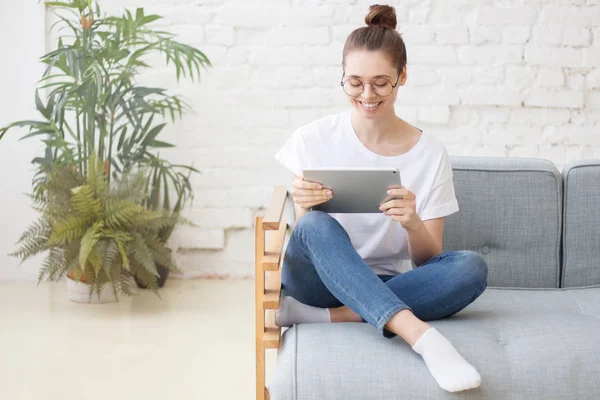 Koncept E-commerce zákazníka. Mladá hospodyňka sedí doma na gauči s tabletem, použití pro online nakupování, usmíval se široce — Stock fotografie