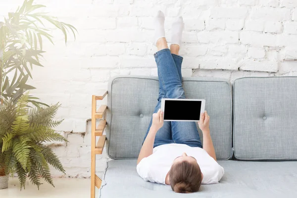 Mladá žena položil na pohovku, relaxační, sledovat něco, co na tabletu — Stock fotografie