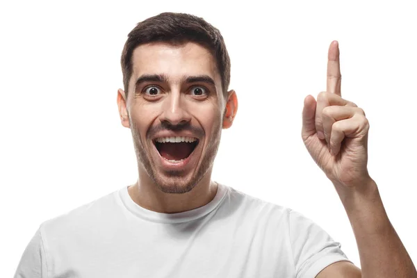 Närbild porträtt av ung stilig leende man i vit t-shirt, pekande fingret i eureka logga, med bra nyskapande idé, förstå lösning — Stockfoto