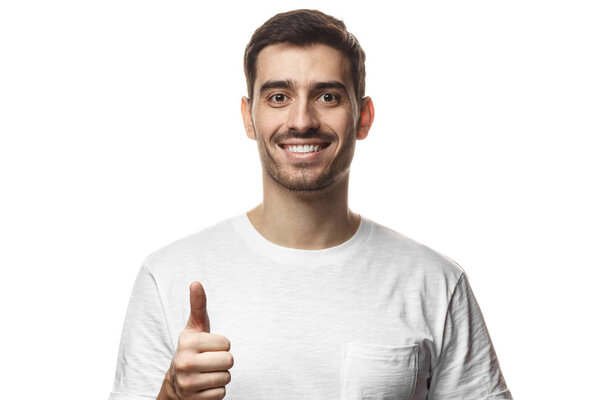 Young optimistic man isolated on white background showing thumb up with positive emotions of content and happiness. Concept of satisfaction with quality and recommendation