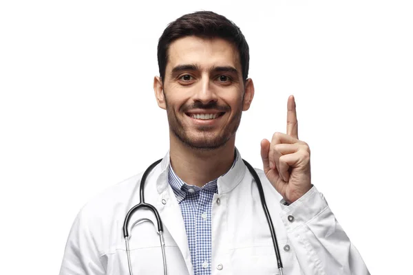 Atractivo joven doctor apuntando hacia arriba con el dedo aislado sobre fondo blanco —  Fotos de Stock