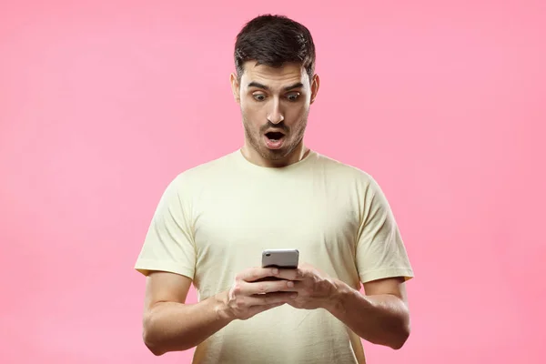 Nahaufnahme Porträt eines gutaussehenden jungen Mannes in beigem T-Shirt, der sein Smartphone in der Hand hält, verängstigt und verwirrt schaut, als er SMS oder E-Mail liest — Stockfoto