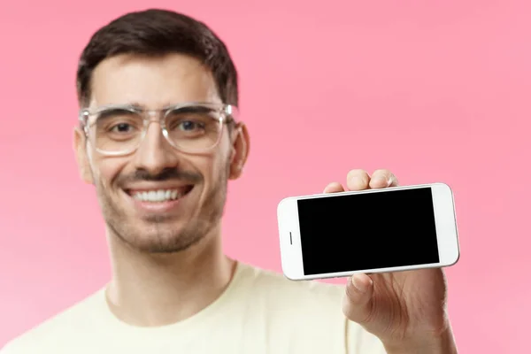 Крупный план молодого красивого мужчины, улыбающегося изолированно на розовом фоне, держащего и показывающего горизонтальный пустой смартфон с копирайтом для рекламы приложений, сайтов, товаров и услуг — стоковое фото