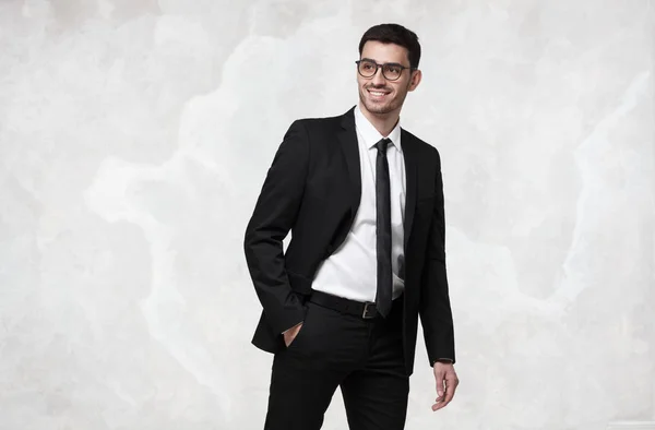 Elegante joven hombre de negocios sonriente caminando contra la pared de textura gris — Foto de Stock