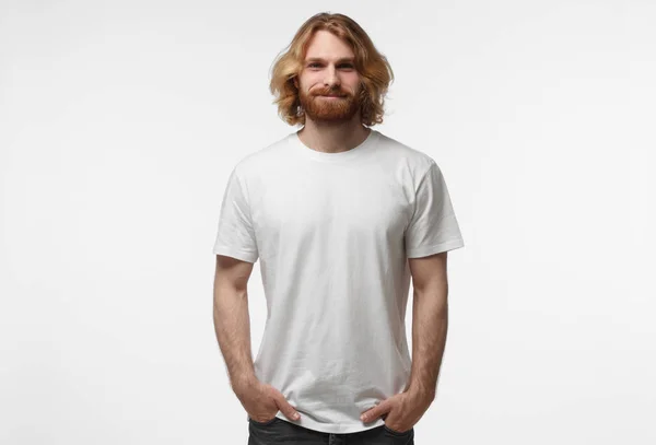 Young european smiling man standing with hands in pockets, wearing blank white tshirt with copy space isolated on grey background — Stock Photo, Image