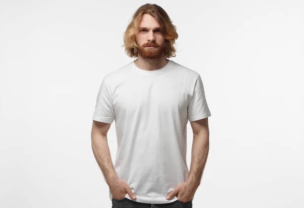 Elleri ceplerinde duran, logo veya metin, gri arka plan üzerinde izole kopya alanı olan beyaz tshirt giyen genç Avrupa erkeksi adam — Stok fotoğraf