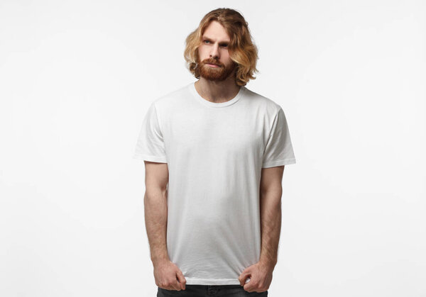 Young european man standing isolated on grey background, wearing blank white tshirt with copy space for your logo or text