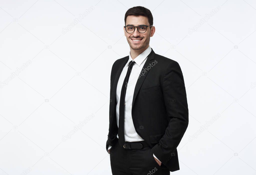 Indoor picture of young business man in glasses pictured isolated on grey background looking straight at camera, showing confidence and providing stability for employees