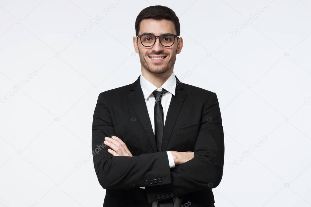 Portrait of smiling handsome business man standing with crossed arms isolated on grey background