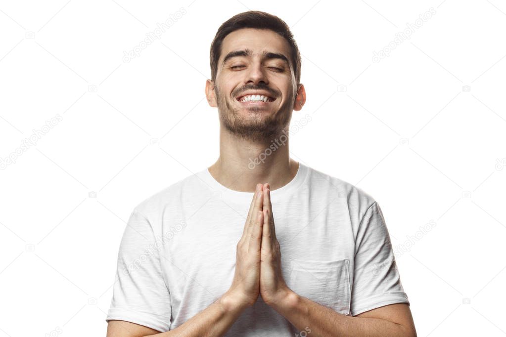 Young smiling man isolated on white background, having put hands together in prayer or meditation, dreaming and waiting for all best on exam