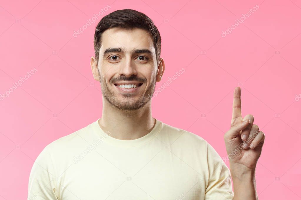 Attractive young man in white t-shirt pointing up with his finger isolated on pink background